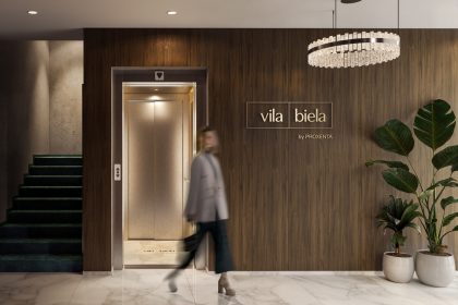 Проект Vila Biela: Холл у лифта с тёмной деревянной стеной, лестницей и крупными растениями