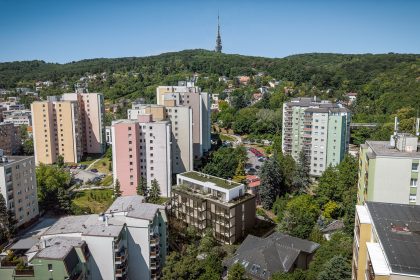 Проект Vila Magurská: Вид сверху на тёмный корпус среди многоэтажных домов и лесистого холма
